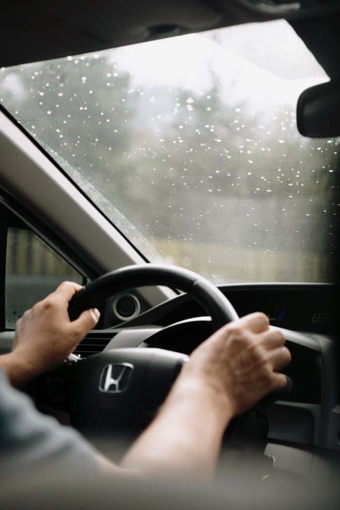 Close-up of hands on a steering wheel driving on a rainy day.